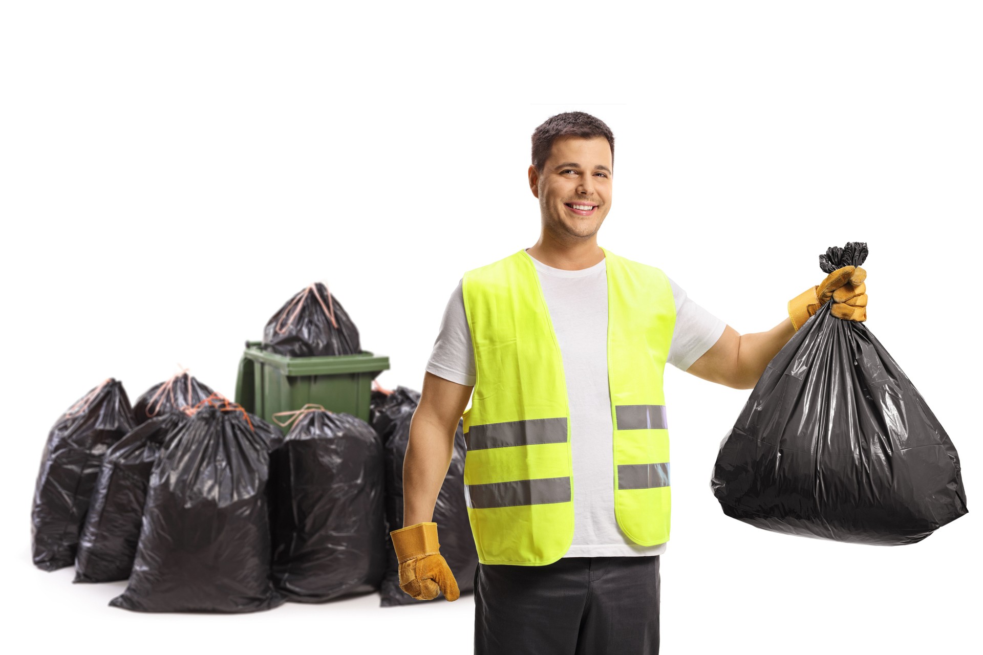 Waste collector holding a plastic bag in front of a bin and a pile of bags and smiling at camera